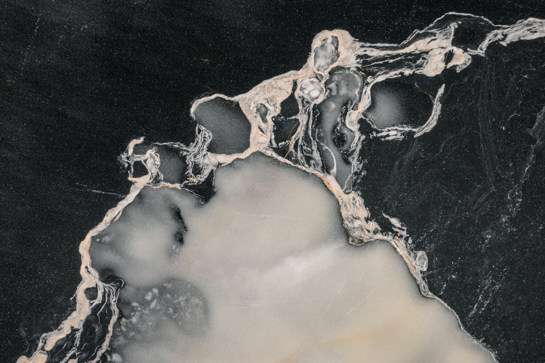 Abstract textures and patterns on the dark ice surface of a frozen lake in Norway