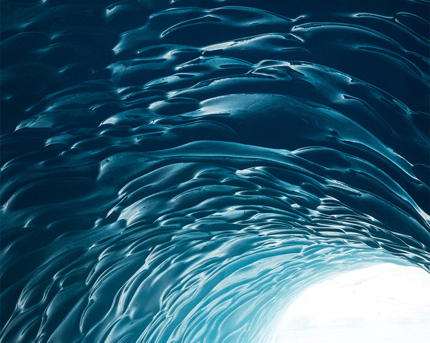 The inside of a frozen iceberg tunnel in Iceland, showing polished surfaces and intense blue tones