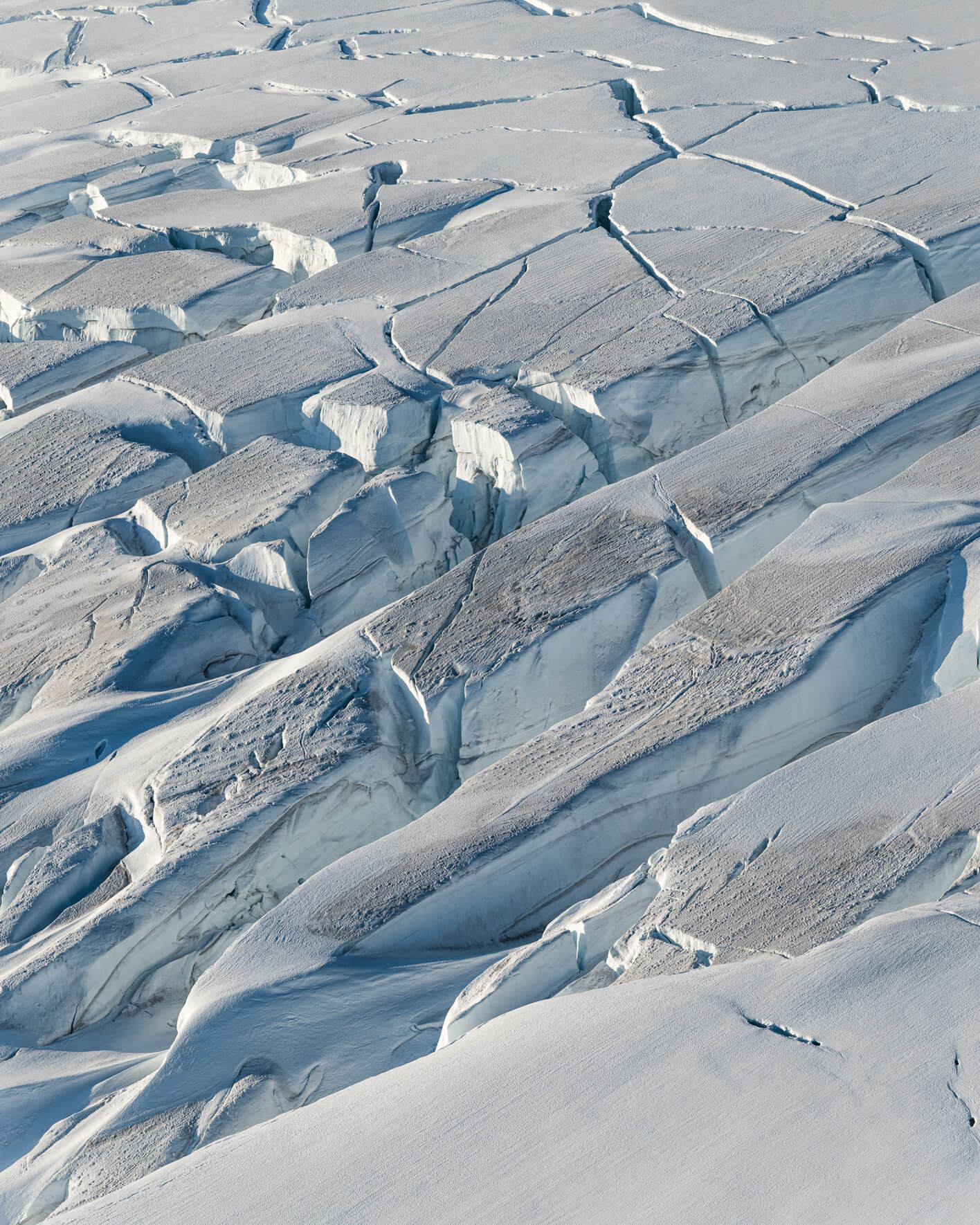 Aerial view of snow-covered glacier surface with elongated crevasses