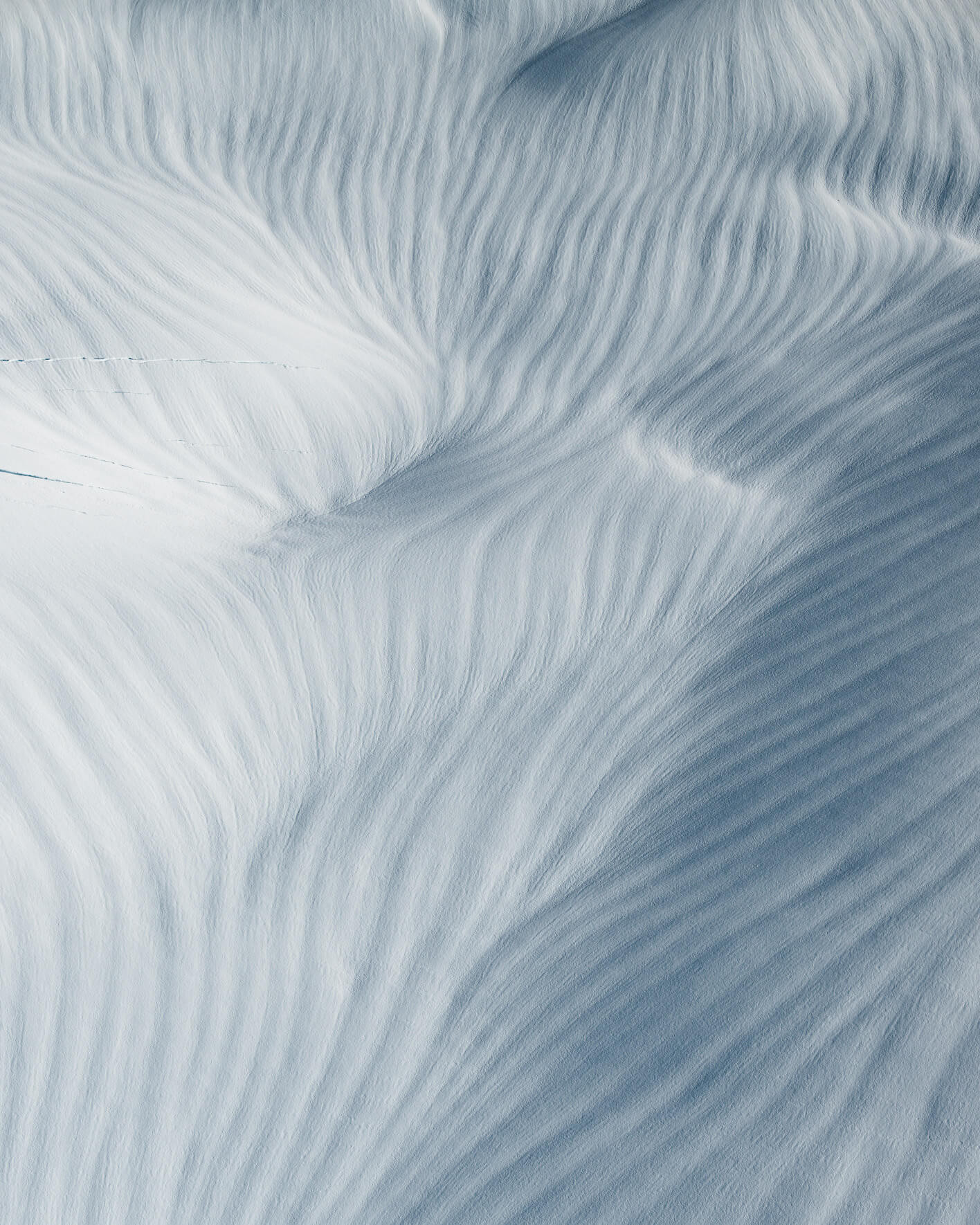 Aerial view of smooth snow formations creating organic wave-like glacier patterns