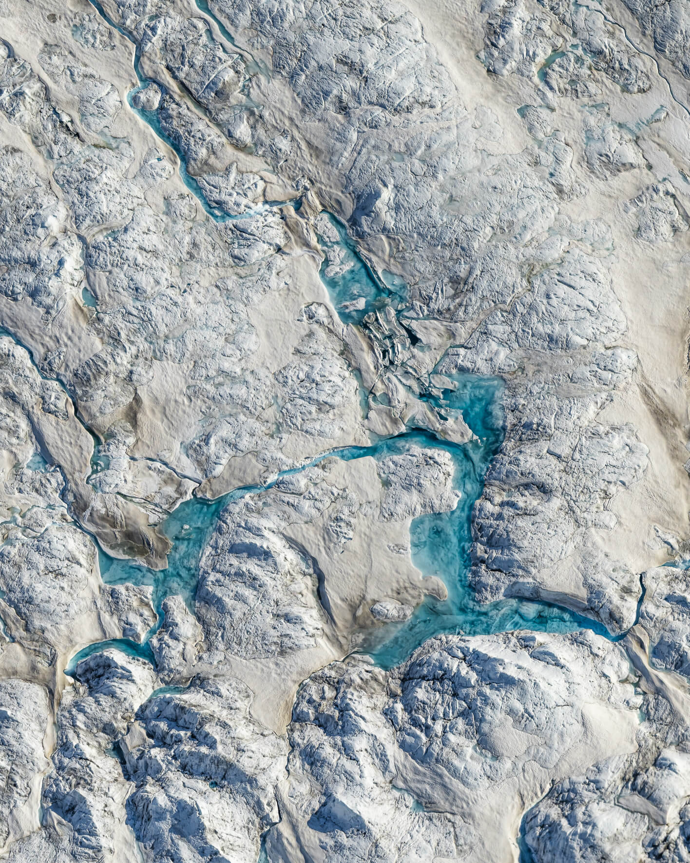 Aerial view of bright blue meltwater channel cutting through white glacier snow.