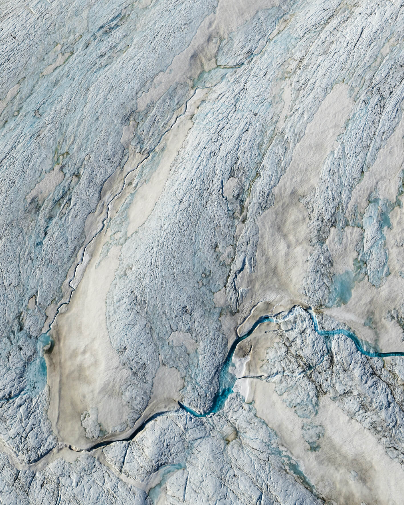 Aerial view of bright blue meltwater channel cutting through white glacier snow