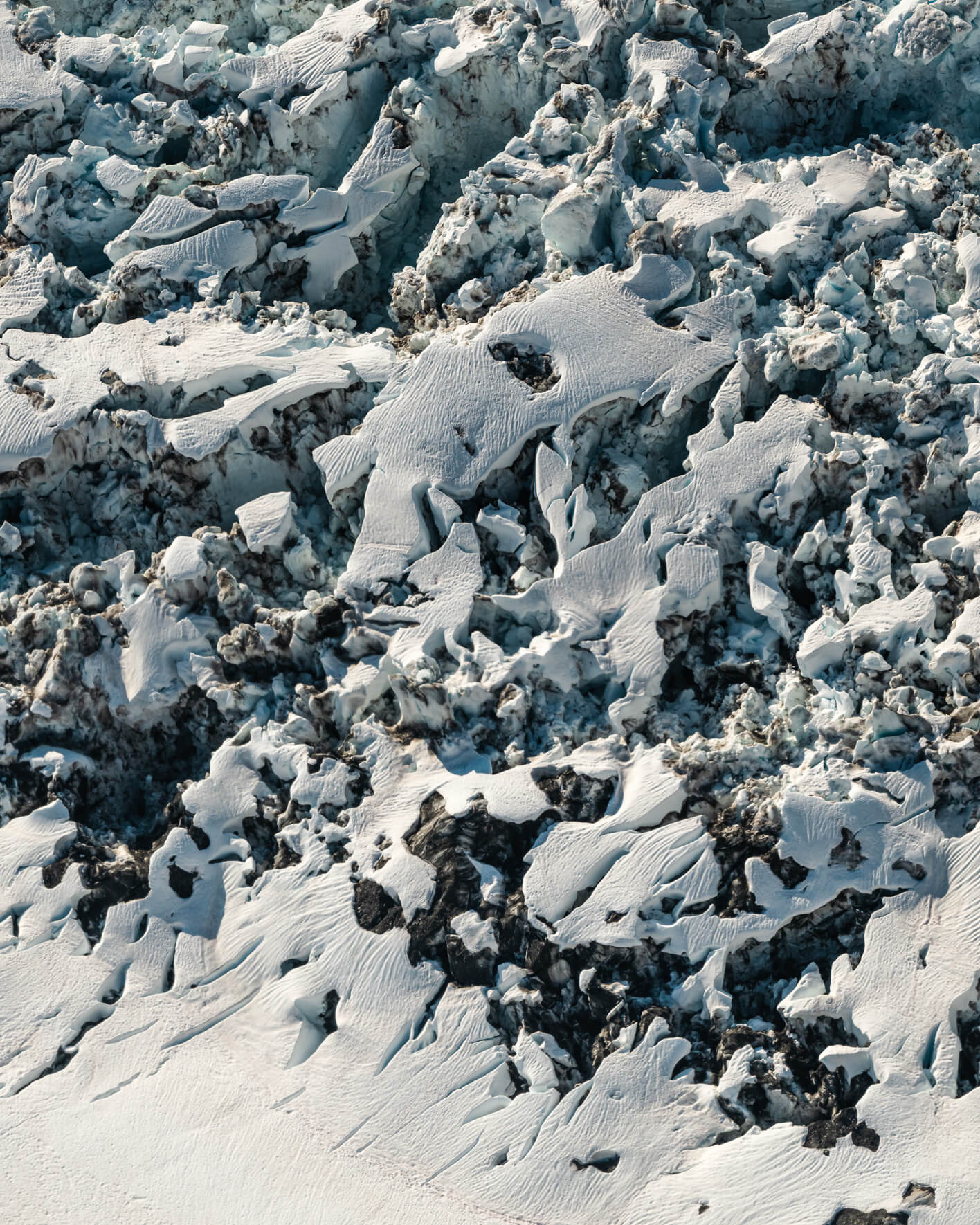 Aerial view of fractured glacier surface with broken ice blocks and sculpted snow