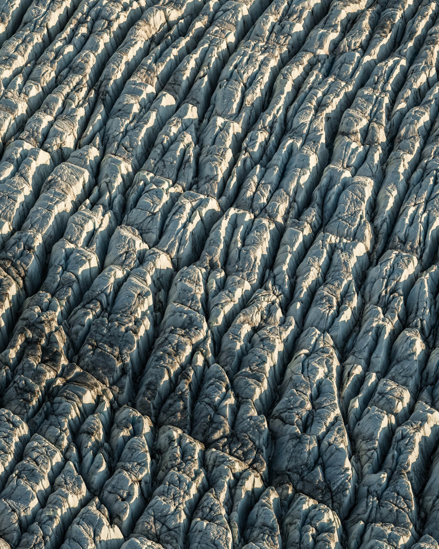 Aerial view of jagged glacier surface with snow-covered ridges and deep crevasses.