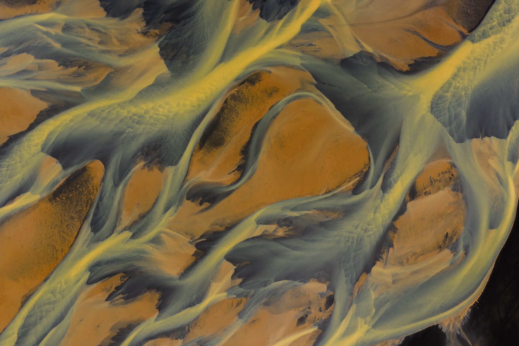 Aerial view of yellow glacial river forming abstract volcanic patterns