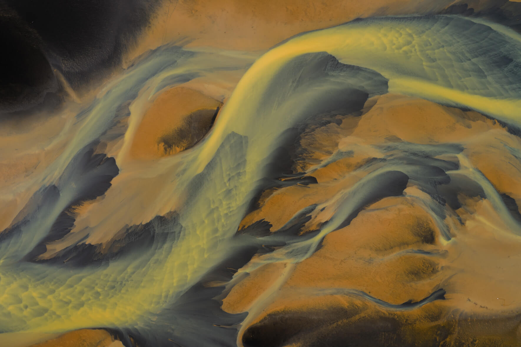 Aerial view of sulphur-rich river in Iceland with golden geothermal tones and black sand