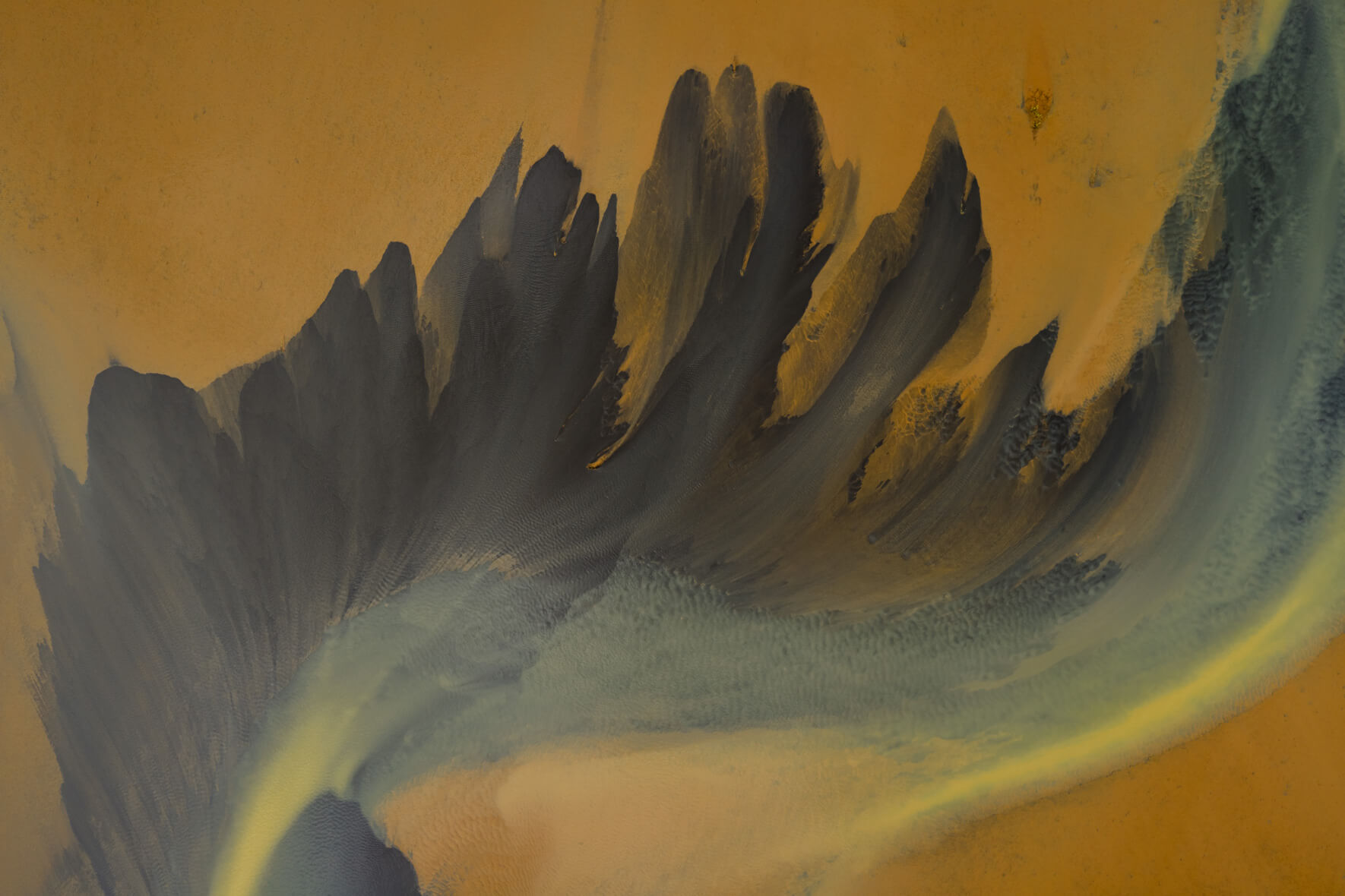 Aerial view of geothermal runoff creating dark abstract patterns on orange sediment