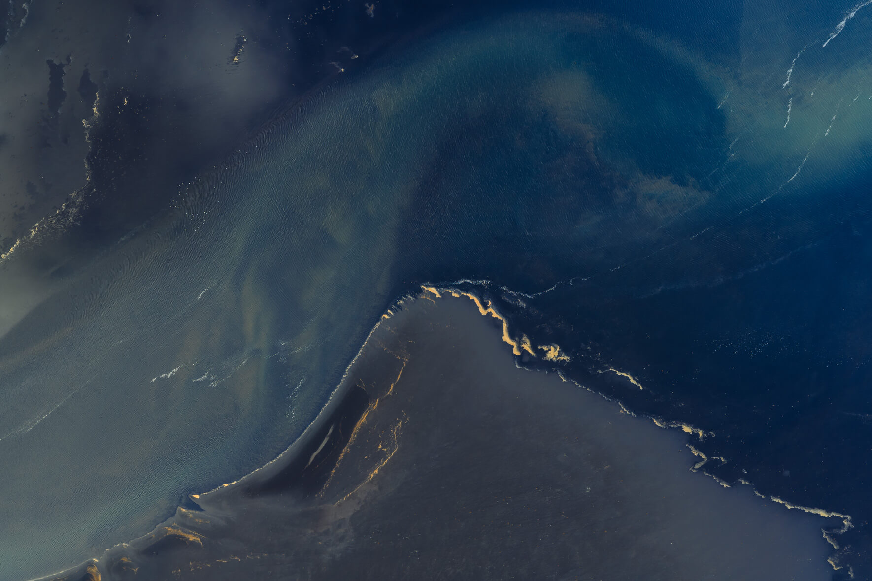 Aerial view of Icelandic lagoon with organic foam glowing gold against dark tidal water