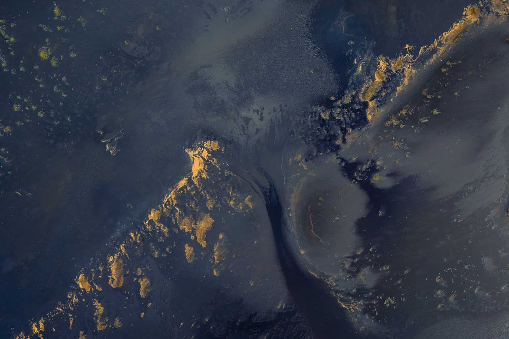 Aerial view of lagoon surface in Iceland with gold-tinted foam drifting across dark water