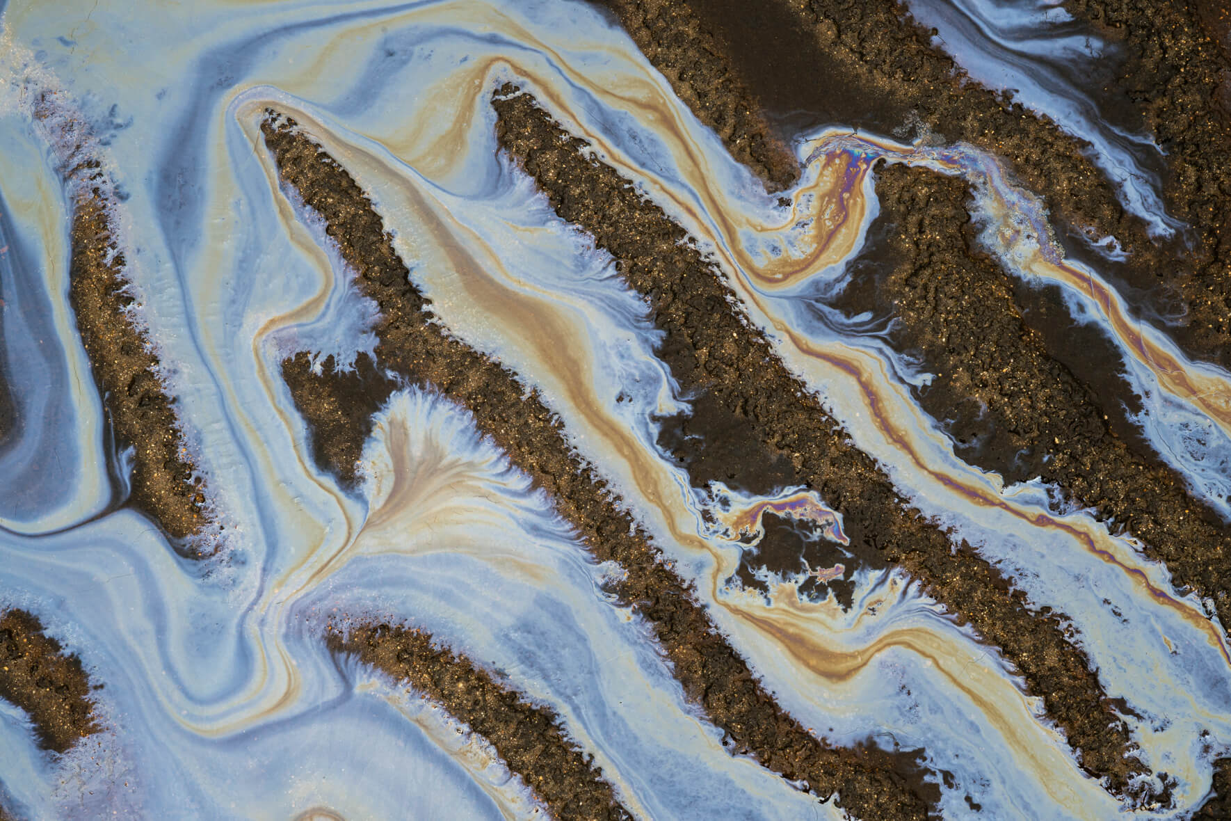 Close-up of iridescent iron bacteria film on sand and mud