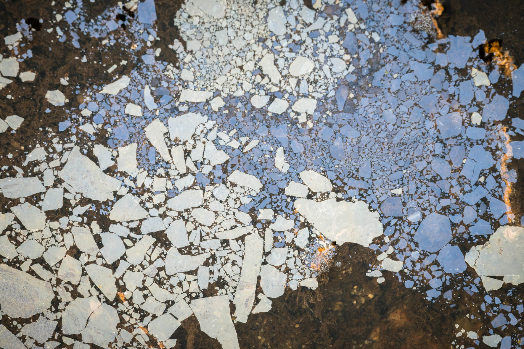 Colorful oxidized layer on shallow water surface showing natural metallic reflections