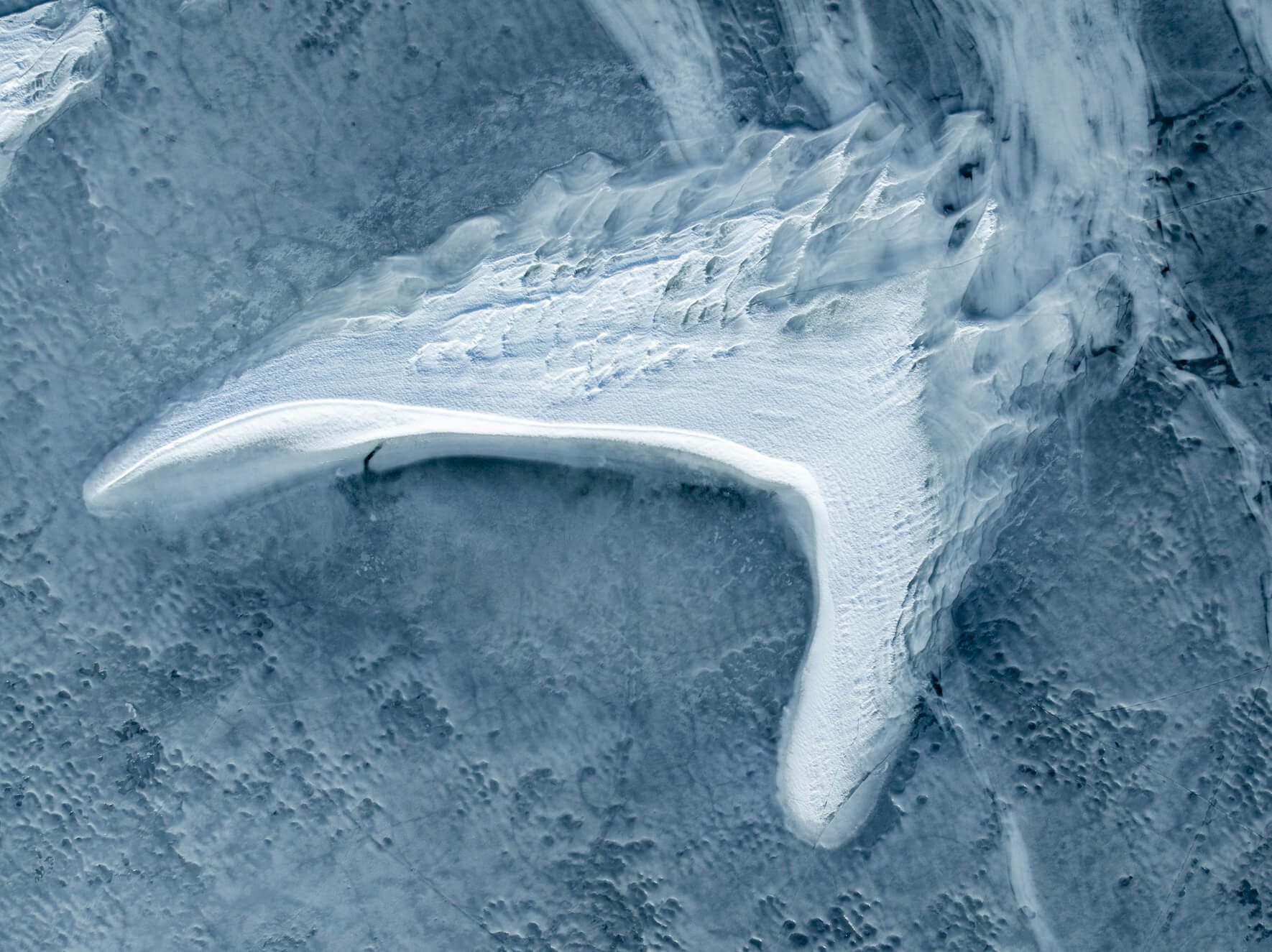 Frozen lake textures with sweeping snow curves resembling white wings on ice