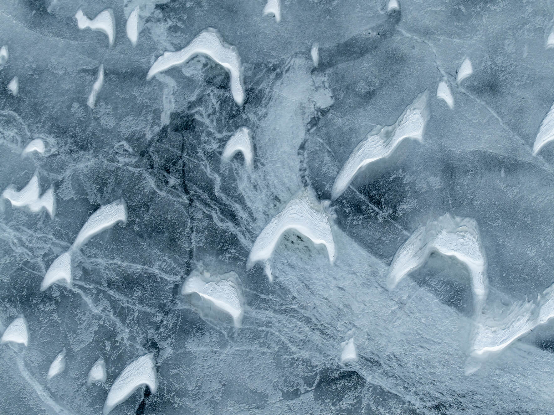 Aerial view of Norwegian lake with cracked ice and melting snow patterns shaped like wings